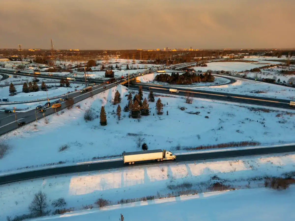 A semi-truck crossing a snow-covered highway interchange in North America at sunset